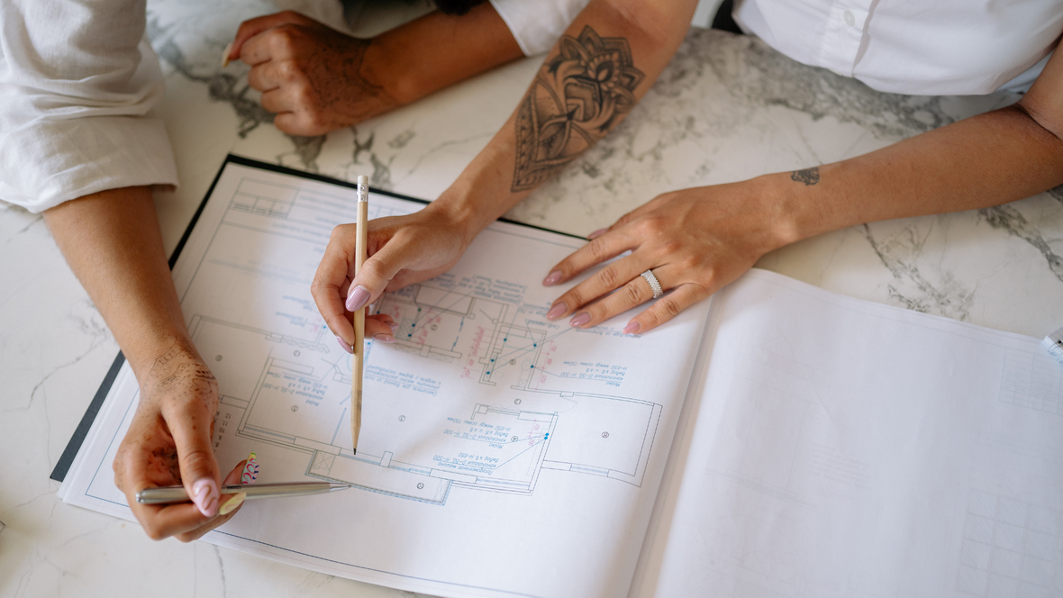 Zwei Personen arbeiten gemeinsam an Architekturplänen auf einem Tisch aus Marmor.